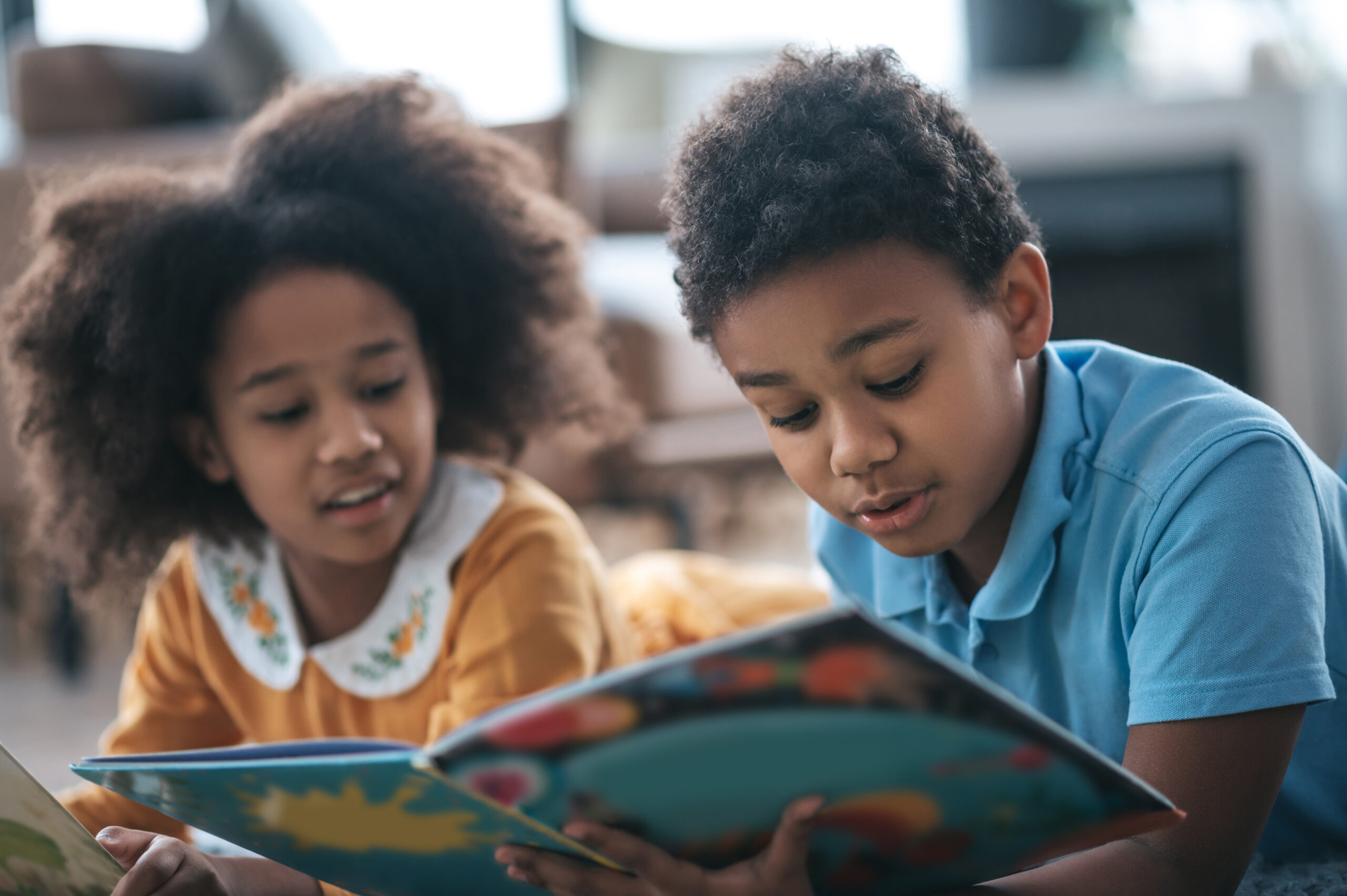 Two kids lying on the floor and reading a book